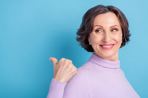 侧面肖像照片，年长女性面带快乐积极的微笑，竖起大拇指，空白空间可用于广告选择促销，背景为蓝色。图片下载