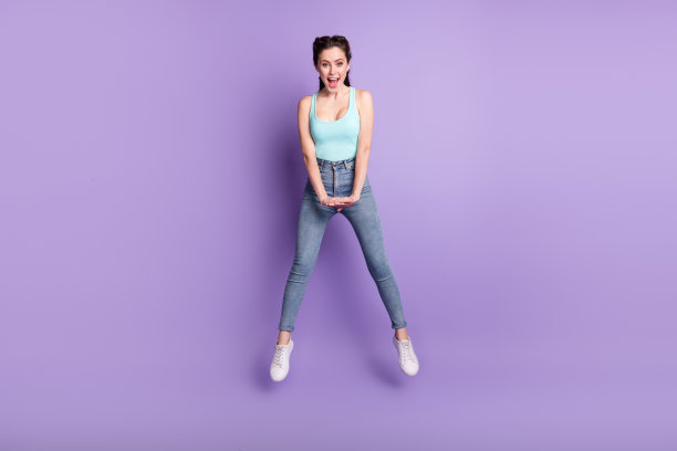可爱的棕发女孩穿着蓝色上衣在紫色背景上跳跃的全身照片图片下载