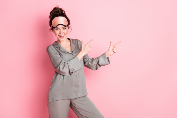 穿着睡衣的女孩微笑着指向空白区域，推荐的照片肖像，背景为柔和的粉色。图片下载