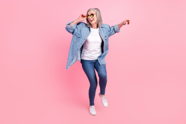 戴着太阳镜的迷人积极老年女性，热爱音乐，独自在粉色背景上跳舞的照片图片下载