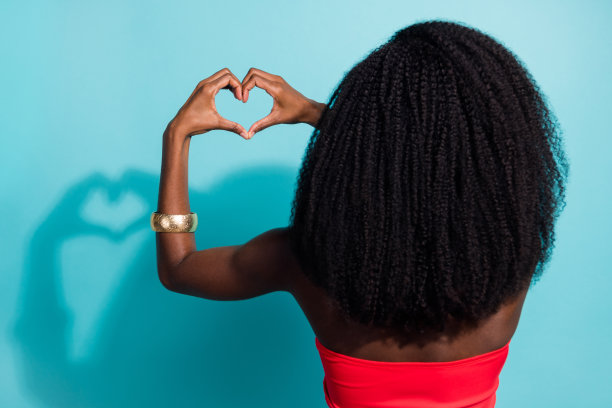 深肤色年轻女性背面脊柱视角照片，双手做心形，背景为青色。图片下载