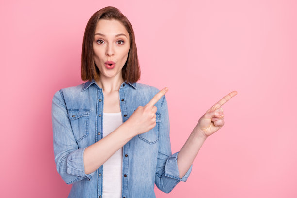 女孩惊讶地指着空白空间，推荐在孤立的粉色背景前拍摄的肖像照片图片下载