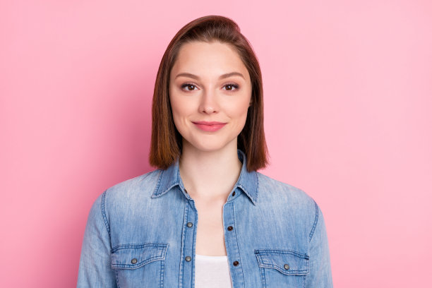 穿着牛仔服的可爱女孩的照片肖像，留着短发，微笑着，背景为柔和的粉色。图片下载