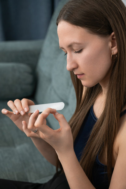 年轻女性舒适地坐在沙发上，专注地用玻璃指甲锉修整指甲，享受着放松的家庭美甲时光，作为她美容程序的一部分。竖版照片图片下载