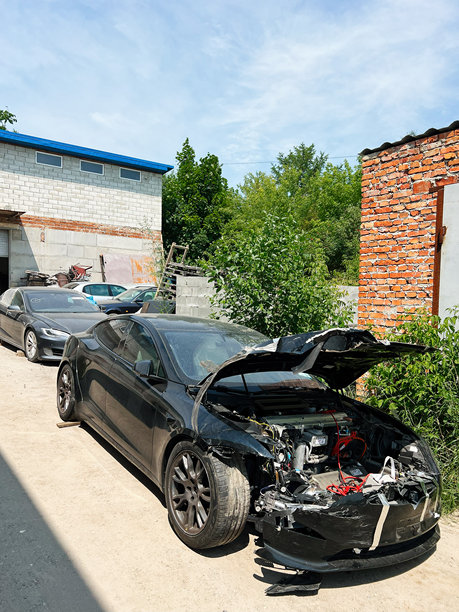 受损的黑色特斯拉汽车停在户外，靠近砖墙和工业建筑。图片下载
