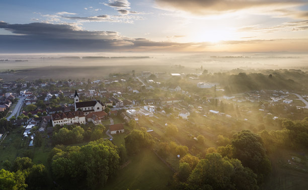 雾霭中的日出无人机照片，森林、湖泊和村庄 - 金色阳光透过光束和阴影。图片下载