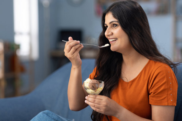 年轻女性坐在家里的沙发上吃冰淇淋的库存照片图片下载