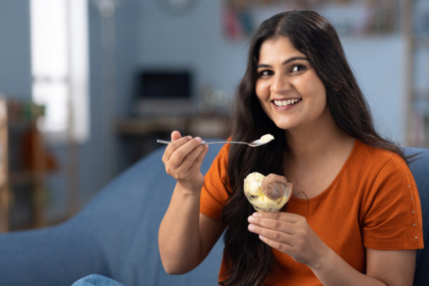 年轻女性坐在家里的沙发上吃冰淇淋的库存照片图片下载