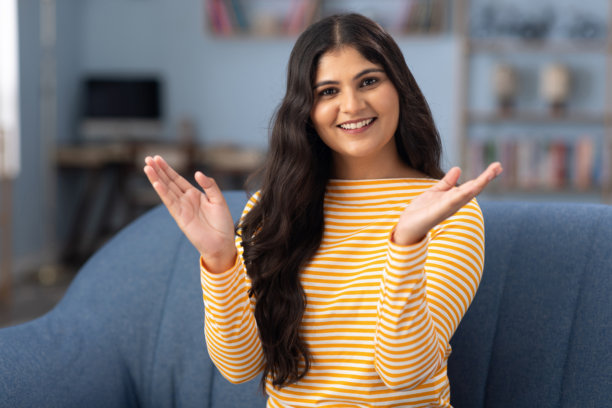 美丽的女性在家中坐在沙发上看着镜头微笑，正在进行视频通话的照片图片下载