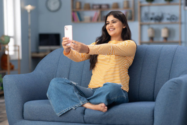 年轻女性穿着现代服装坐在家里的沙发上使用手机的照片图片下载