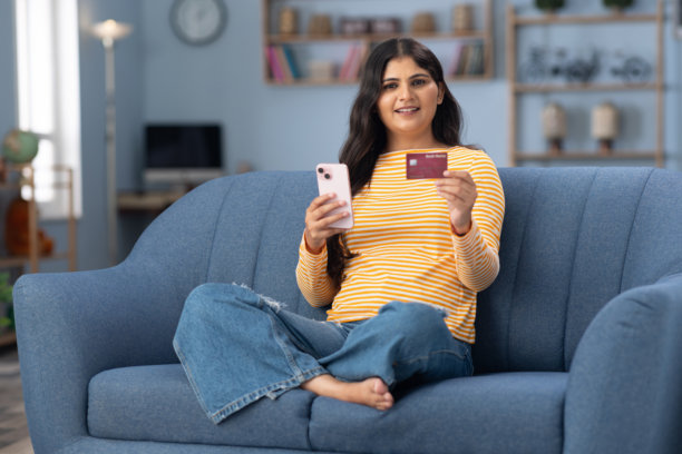年轻女性穿着现代服装坐在家里的沙发上使用手机的照片图片下载