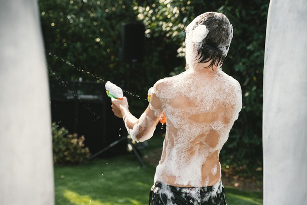 男孩在户外玩水枪，身上覆盖着泡泡图片下载