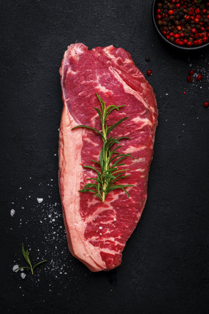 美味的生皮卡尼亚牛排，来自带有脂肪垫的雪花牛肉，配以迷迭香和胡椒，黑色背景。俯视图。图片下载