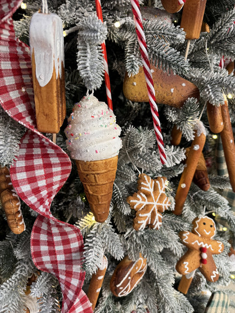 垂直照片特写，展示一个姜饼冰淇淋装饰品，系着红色格子丝带，悬挂在圣诞树上，为节日装饰增添温暖而喜庆的氛围。图片下载