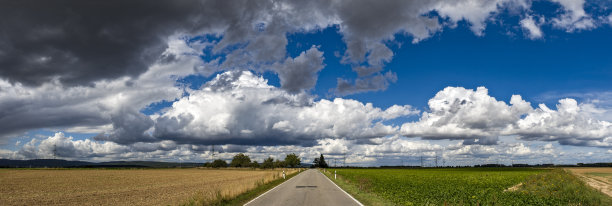 一幅全景照片，展示了暴风雨横扫全国，乌云密布，伴随着大雨倾泻在农田和乡村道路上。图片下载
