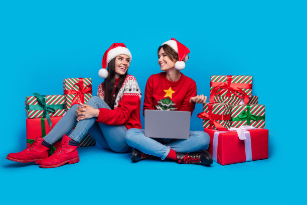 兴奋的时尚女性圣诞精灵穿着装饰性毛衣，在蓝色背景下挑选圣诞礼物的全身照片图片下载