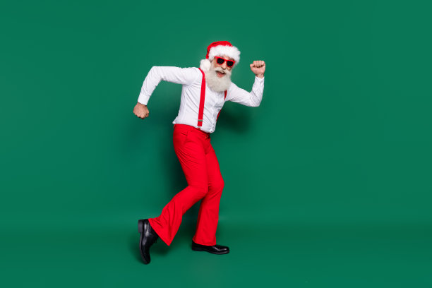 穿着圣诞服装的积极老年男士，戴着眼镜，在空旷的绿色背景下快乐地跳舞的全身照片图片下载