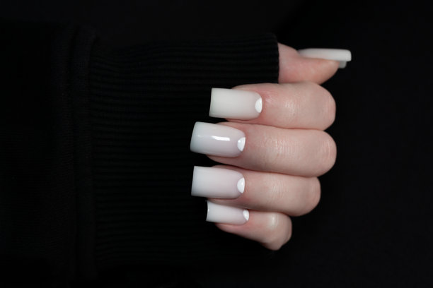 现代美甲，光滑的白色指甲搭配时尚设计。女性手臂穿着黑色袖子，展示优雅的美甲。美学照片展现美容院、指甲油、优雅和专业的指甲护理。图片下载