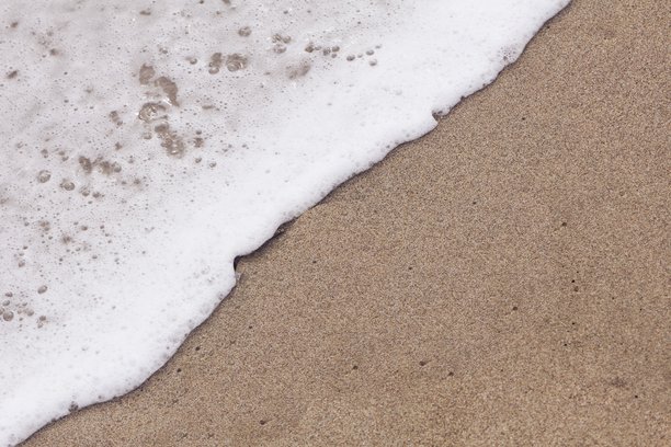 阳光明媚的小沙滩上柔和的海浪，适合用于横幅和卡片的文本空白。海蓝色的波浪在沙滩上轻轻拍打，照片拍摄于黄昏时分。图片下载