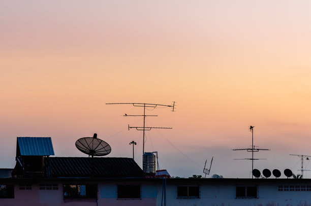老式卫星天线和复古风格的电视天线在日落天空中的建筑屋顶上。图片下载