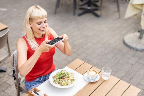 微笑的年轻女性在户外咖啡馆拍摄食物照片图片下载