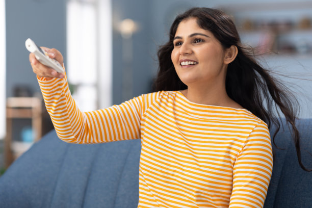 快乐的年轻女性在时尚的家中调节空调，享受阳光明媚的室内舒适与放松时光的照片图片下载