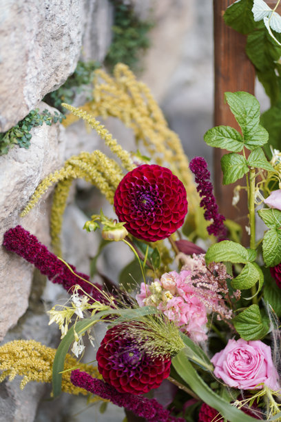 生机勃勃的大丽花和玫瑰花束特写，旁边有绿色植物，背景是一面石墙。图片下载