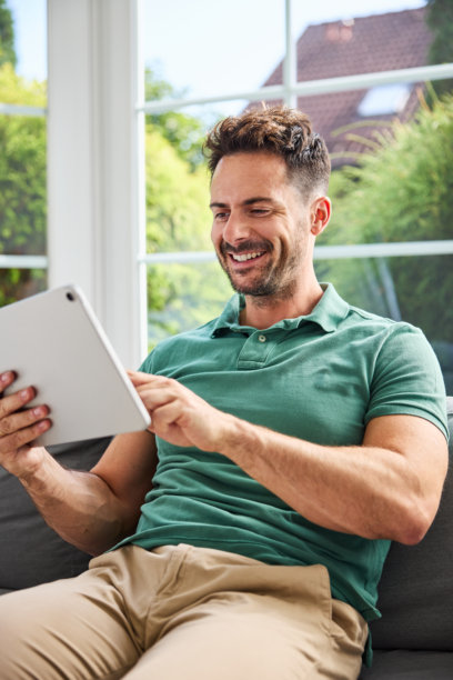 成年男子在家中坐在沙发上使用平板电脑的竖版照片图片下载