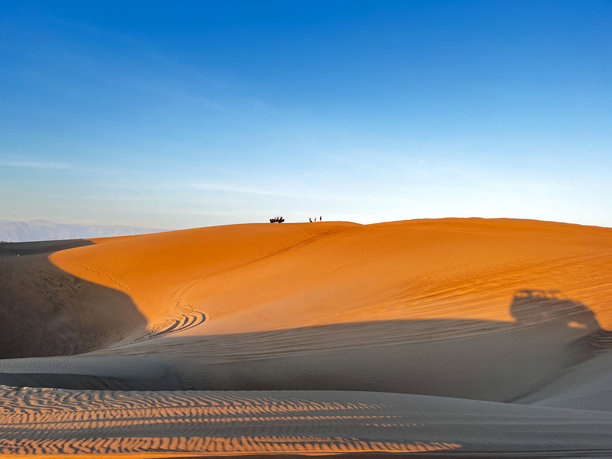 美丽的沙丘在沙漠中，日出日落时分，沙丘顶上有几位游客和越野车进行观光。图片下载