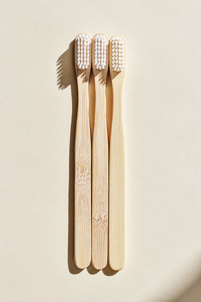 阳光下的米色背景上，环保木质牙刷与白色刷毛。极简风格设计照片，可持续卫生理念，零废弃生活方式，环保意识生活，深色阴影。图片下载