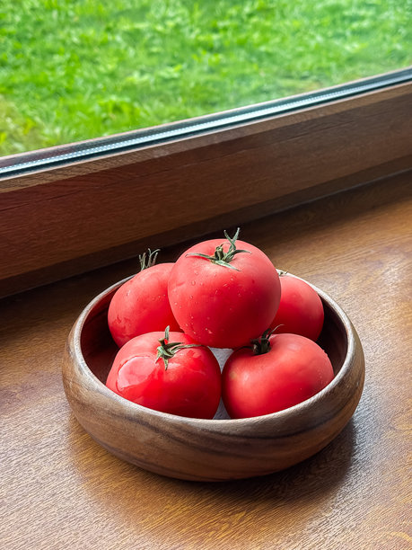 垂直照片：木窗台上放着一个装有番茄的木盘，窗边的环境营造出一种乡村生活的氛围。图片下载