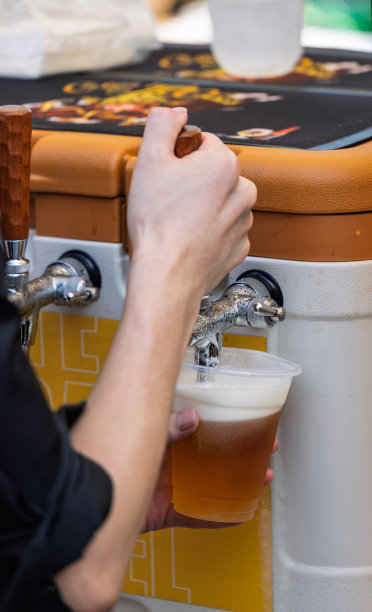 在户外活动中，从水龙头向塑料杯倒生啤酒的人图片下载