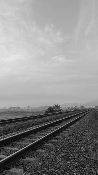 黑白照片显示铁路轨道蜿蜒穿过阴云密布的乡村风景图片下载