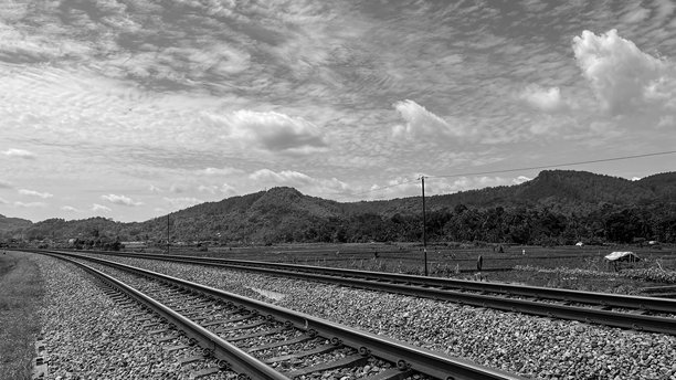 黑白照片展示了铁路轨道在阴云密布的天空下蜿蜒穿过乡村风景。图片下载