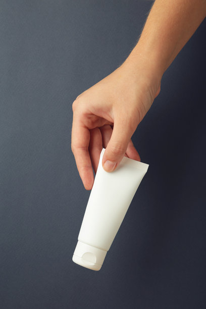 手握空白白色塑料管，背景为深蓝色。化妆品美容产品品牌展示样图。竖版照片图片下载