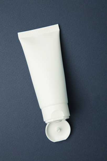 面部护肤白色管瓶，盖子打开，产品置于深蓝色背景上。竖版照片图片下载