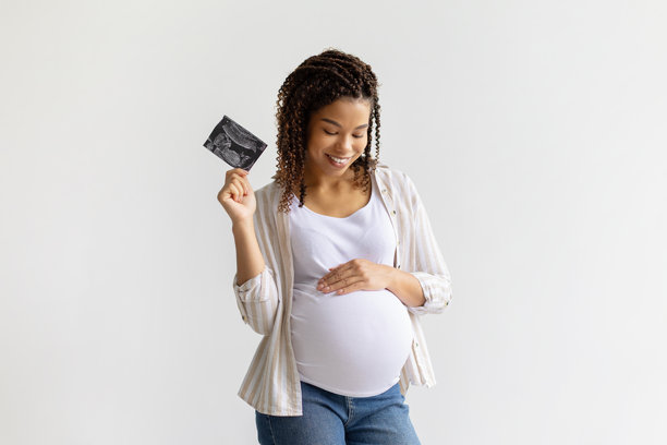 快乐的非裔美国孕妇手持超声波照片，轻抚肚子图片下载
