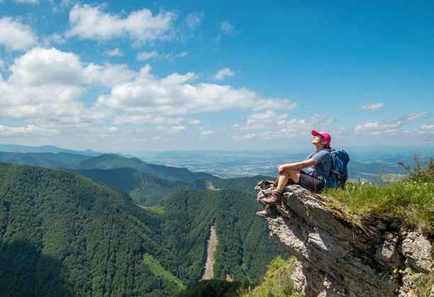 穿着登山服的女性徒步旅行者坐在岩石悬崖上，欣赏斯洛伐克马拉法特拉山脉的绿色山谷。积极生活方式和欧洲旅游概念的图片。图片下载