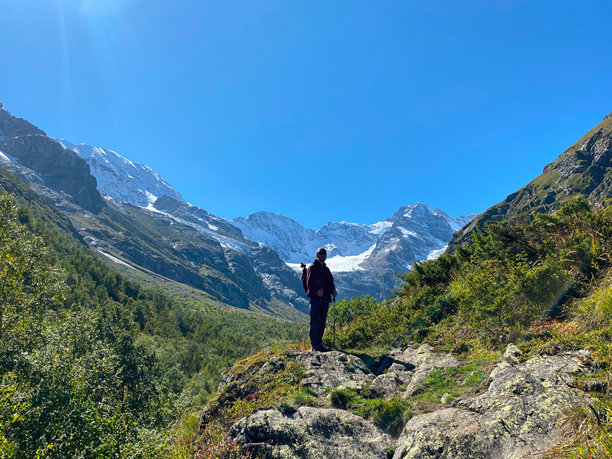 背景山脉的旅游男士，冰川和山坡，山地自然风光与湛蓝的晴空。北奥塞梯的自然景观。带有胶卷颗粒效果的照片。图片下载