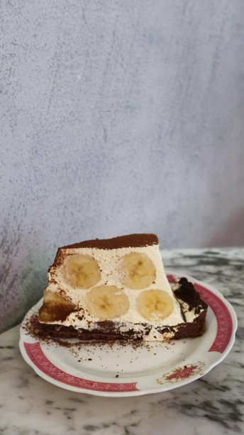 特写垂直照片，展示了一块香蕉提拉米苏蛋糕放在传统中式蛋糕上，背景是大理石桌面。图片下载