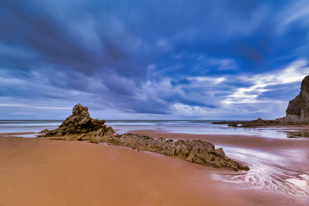 多云的日落映照在崎岖的大西洋海滩上 - 一张长时间曝光的照片，展现了大西洋海岸崎岖岩石海滩上戏剧性的多云日落。图片下载