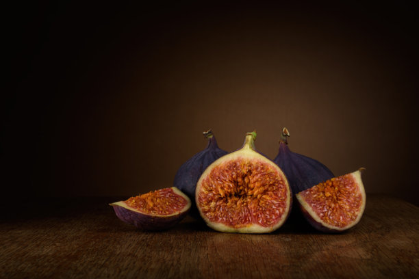 成熟的无花果切片和整颗无花果放在木桌上，背景为柔和的棕色，带有圆形光晕渐变。艺术感十足的黑暗食物照片，留有空白空间。图片下载