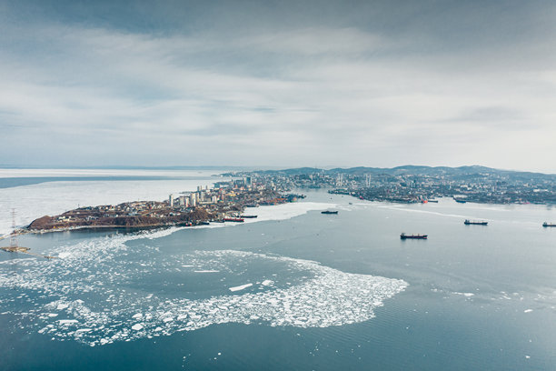 这张航拍照片捕捉了俄罗斯海参崴的冰冷水域和繁忙的港口，展示了其独特的冬季景观。图片下载