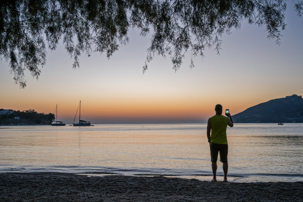 男子在日出时拍摄海洋和帆船的照片图片下载