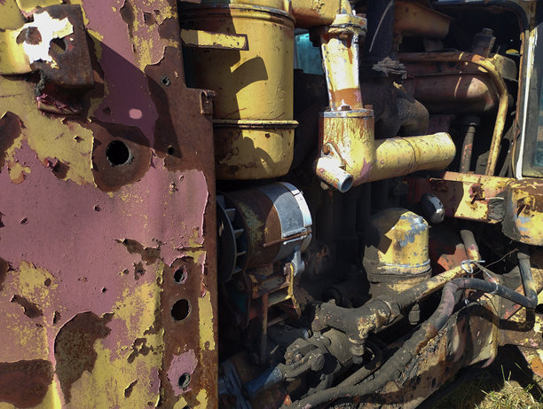 一张宏观照片，展示了一台旧拖拉机生锈且被忽视的机械细节。剥落的油漆、锈迹和污垢象征着时间的流逝，而阳光则突显了形状和纹理的复杂性，将机械转化为抽象。图片下载