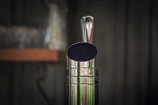 闪亮的啤酒分配塔特写，水龙头把手上有一个空白的圆形徽章。选择性对焦突出了用于酒吧、酒馆和酿酒厂提供生啤的不锈钢设备。图片下载