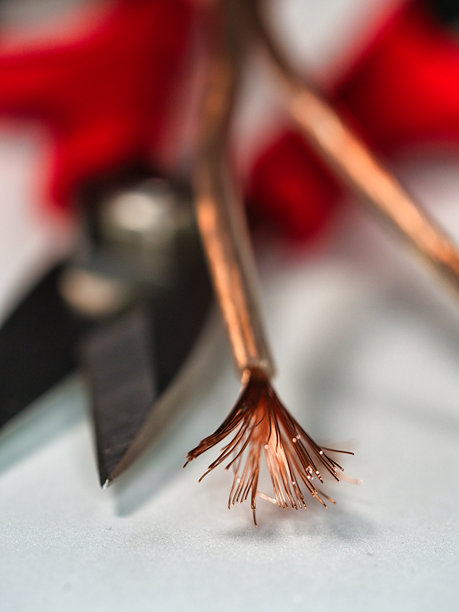 暴露的电缆铜线 - 一张浅景深的照片聚焦于铜电线细致的磨损末端，背景中的工具模糊不清。图片下载