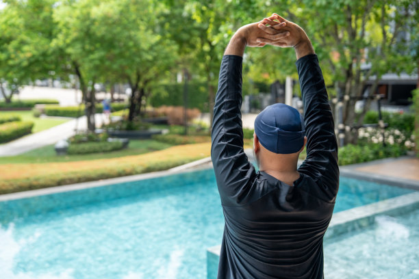 一个穿着黑色泳衣的人在泳池边拉伸，准备游泳。这张图片传达了热身和保持健康积极生活方式的重要性。图片下载