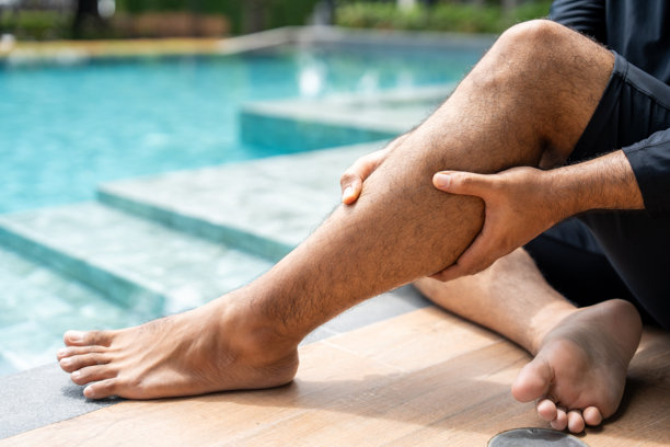 一个人在泳池边按摩小腿，可能感到不适或受伤。这张图片突显了与体育活动相关的常见肌肉问题以及恢复的必要性。图片下载