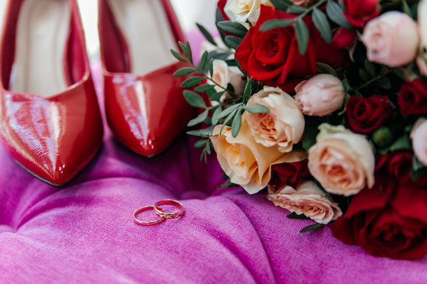新娘的红色漆皮鞋子旁边是金色婚戒和一束玫瑰花。图片下载